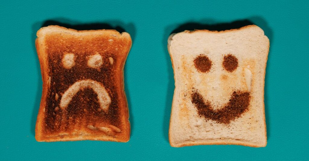 Two slices of toast with happy and sad faces on a teal background.